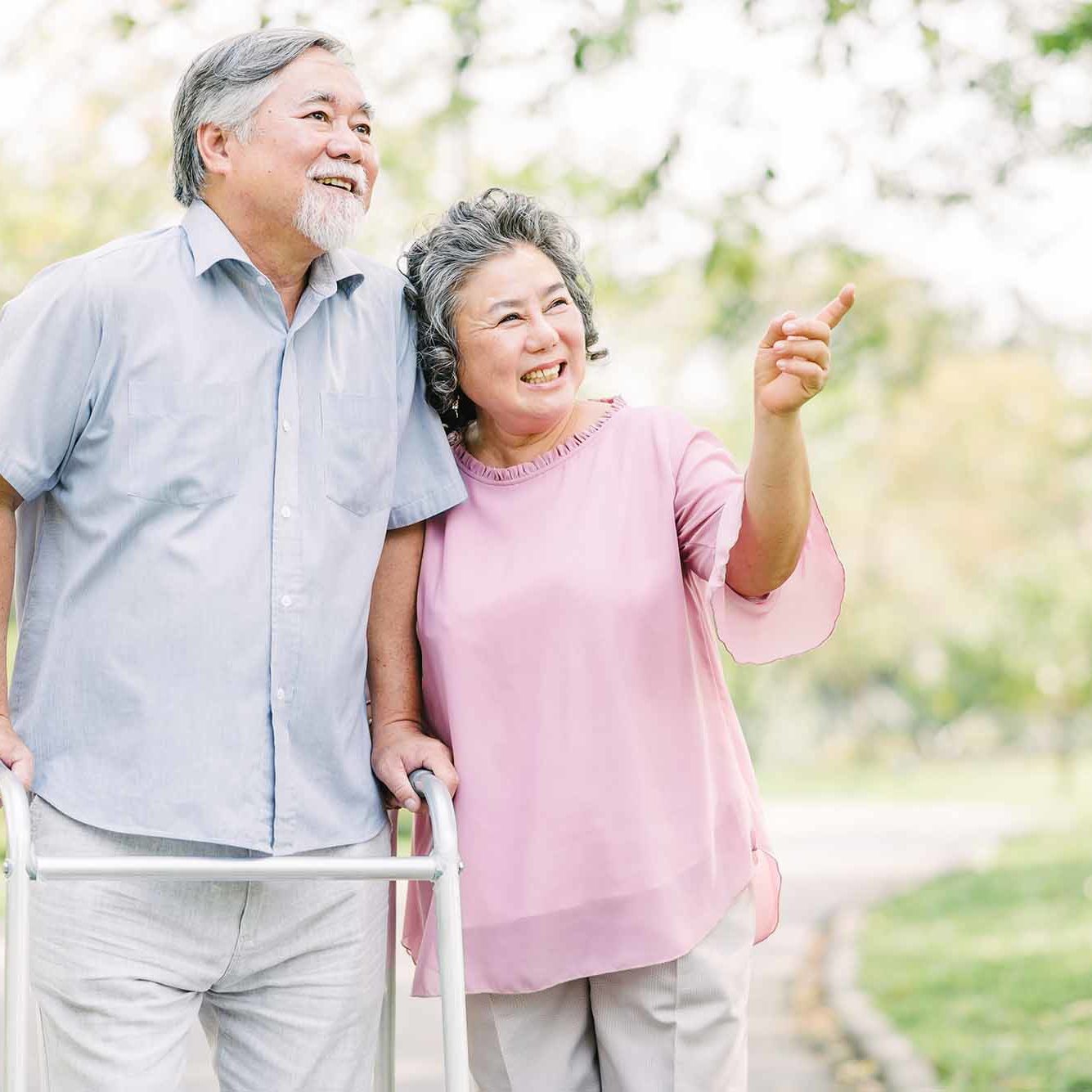 Portrait of happy loving senior Asian couple walking with walker in the park